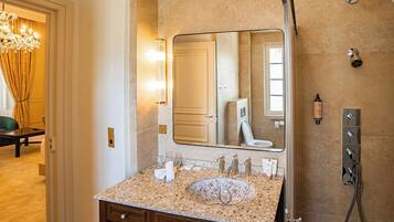 A bathroom with a large mirror, a sink with multiple faucets, a showerhead, and a towel rack.