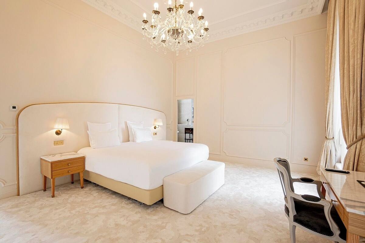 Ein geräumiges Schlafzimmer mit einem großen Bett, einem Holznachttisch, einem Schreibtisch mit Stuhl und einer Chandelüster.