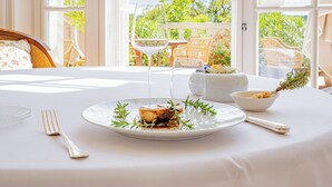 Une table à manger recouverte d’une nappe blanche, une assiette de nourriture, un verre de vin et un saladier.