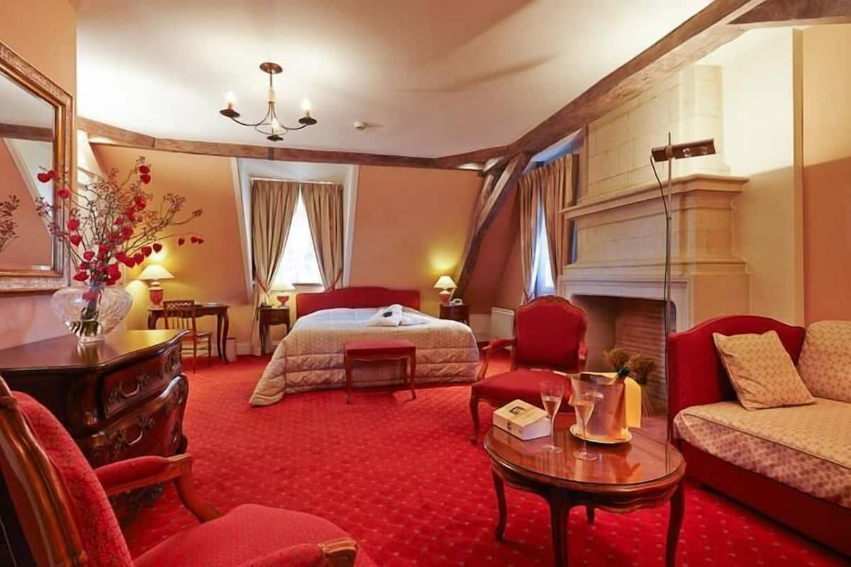 Ein Hotelzimmer mit einem Bett, einem roten Sofa, einem Holztisch, einem Kamin und einem großen Spiegel.