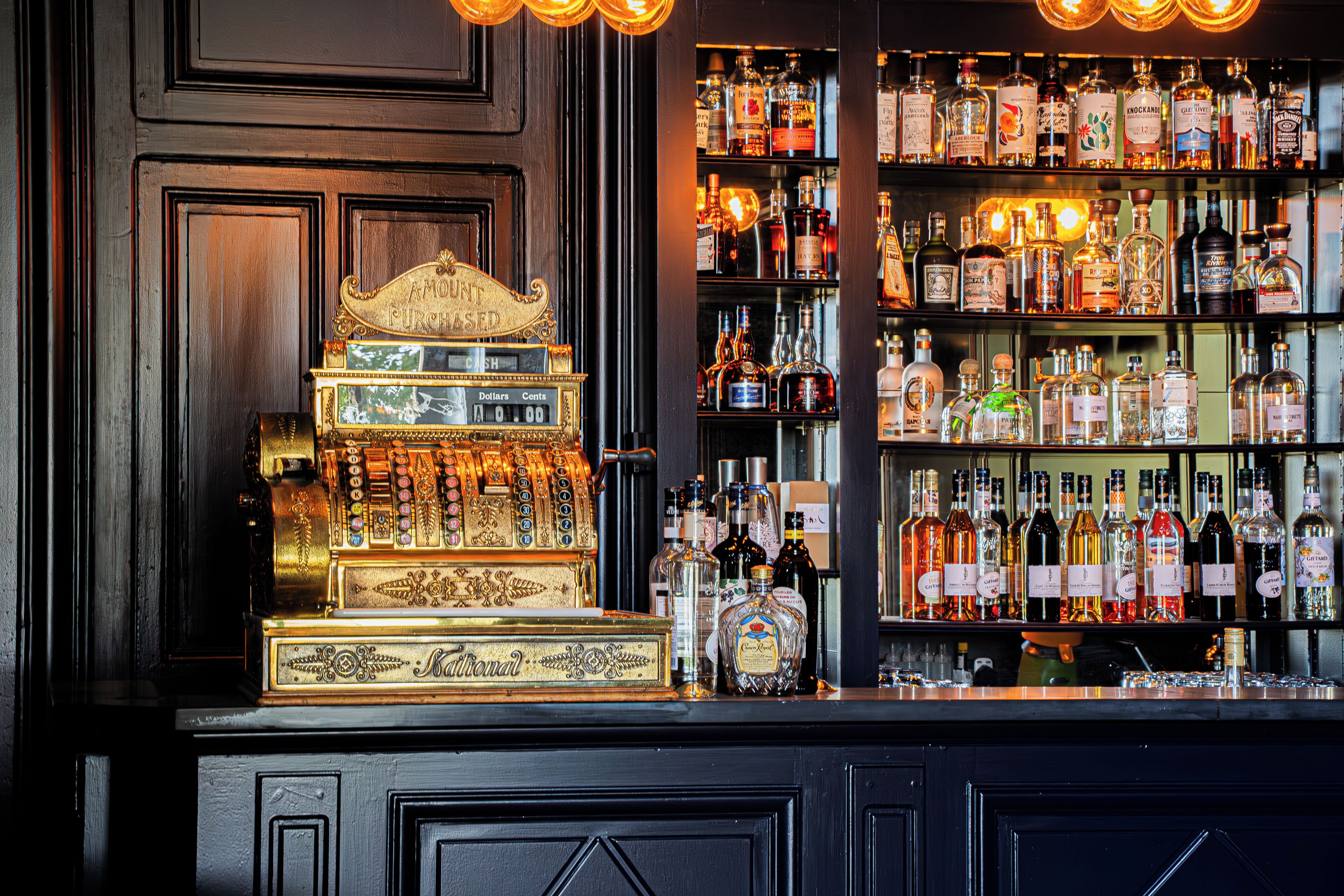 Un bar doté d’une caisse enregistreuse ancienne et d’une étagère bien garnie de bouteilles d’alcool.