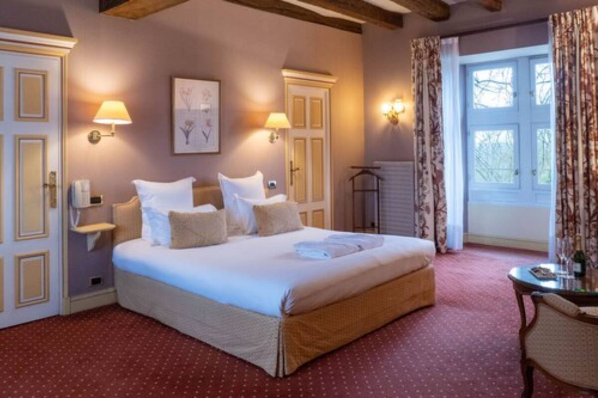 Ein Hotelzimmer mit einem großen Bett, zwei Nachttischen, einem Sessel, einem Fenster mit Vorhängen und Wandlampen.