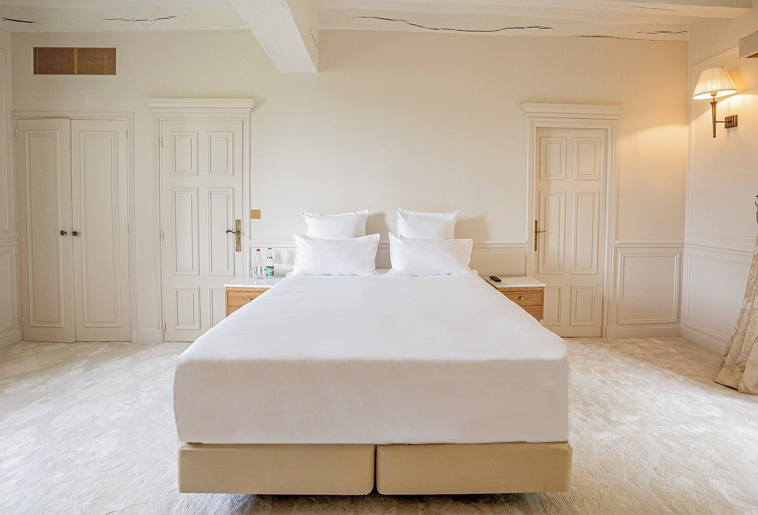 A large bed with white linens in a room with white walls and doors.