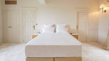 A large bed with white linens in a room with white walls and doors.