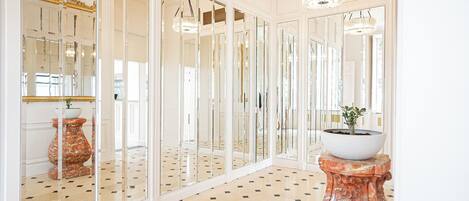 A hallway with mirrored walls, a patterned floor, and a central column with a potted plant.
