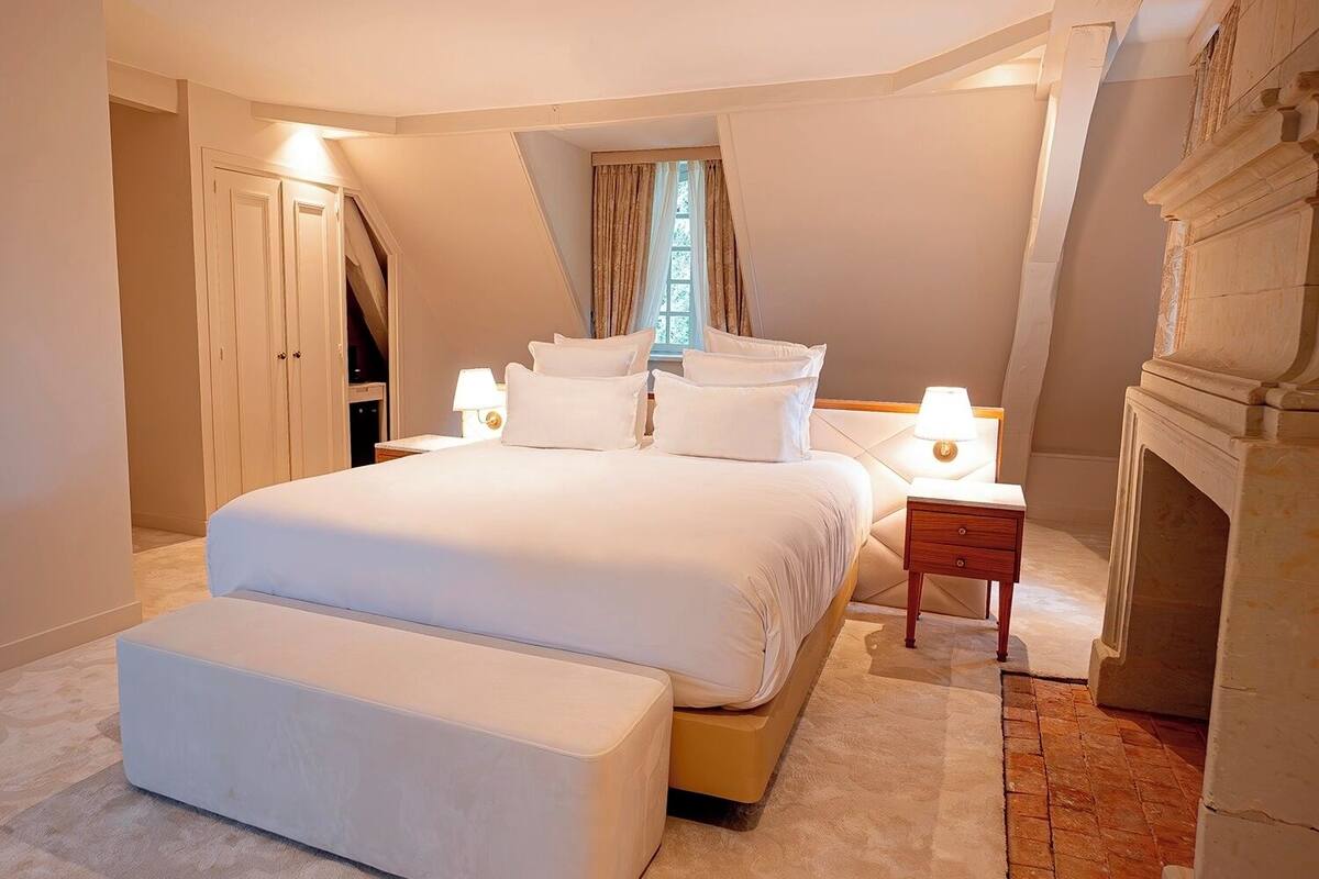 Ein geräumiges Schlafzimmer mit einem großen Bett, einem Nachttisch, einer Bank und einem Kamin.