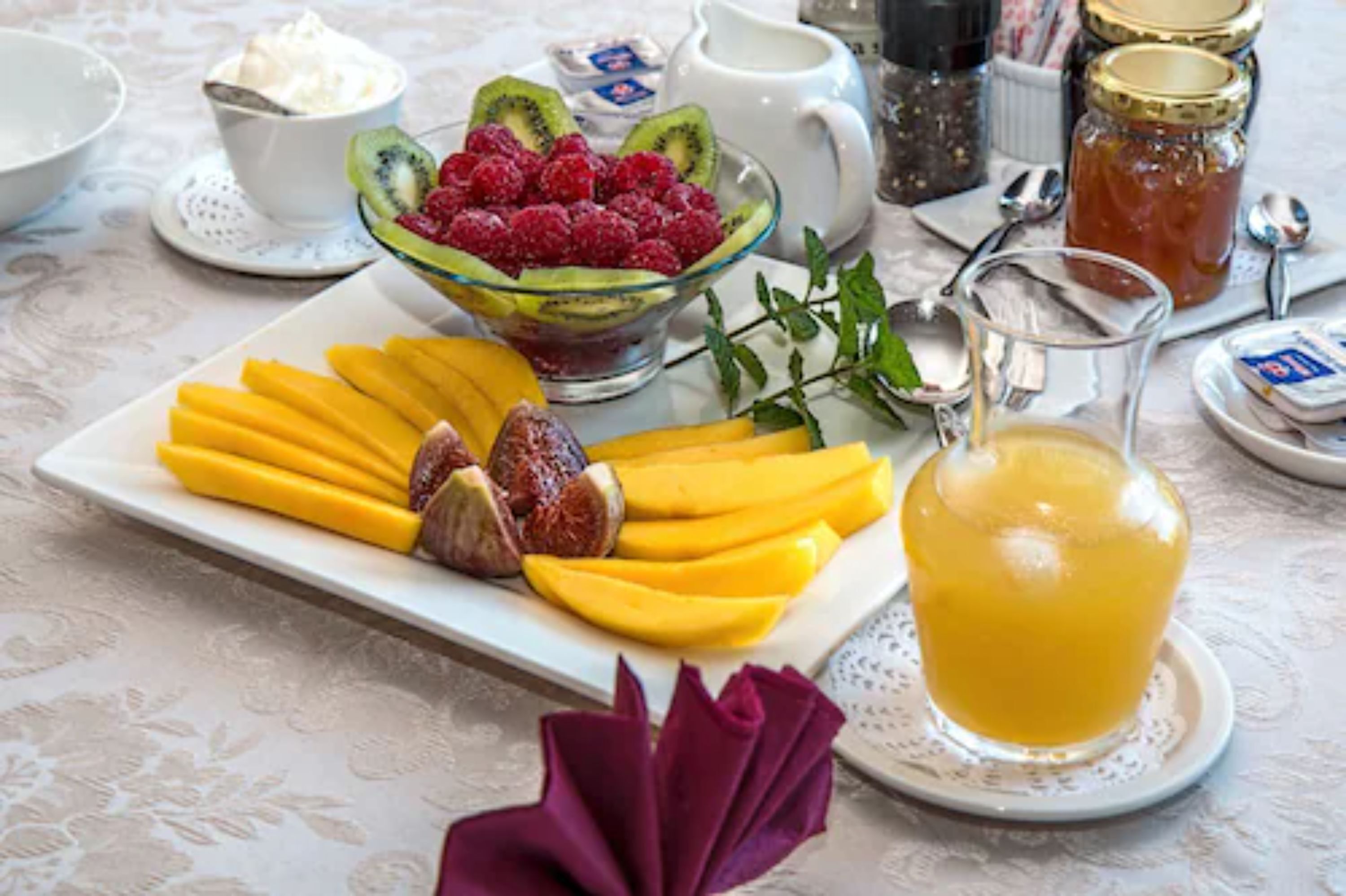 Una mesa con una bandeja de frutas, un vaso de jugo y aderezos.