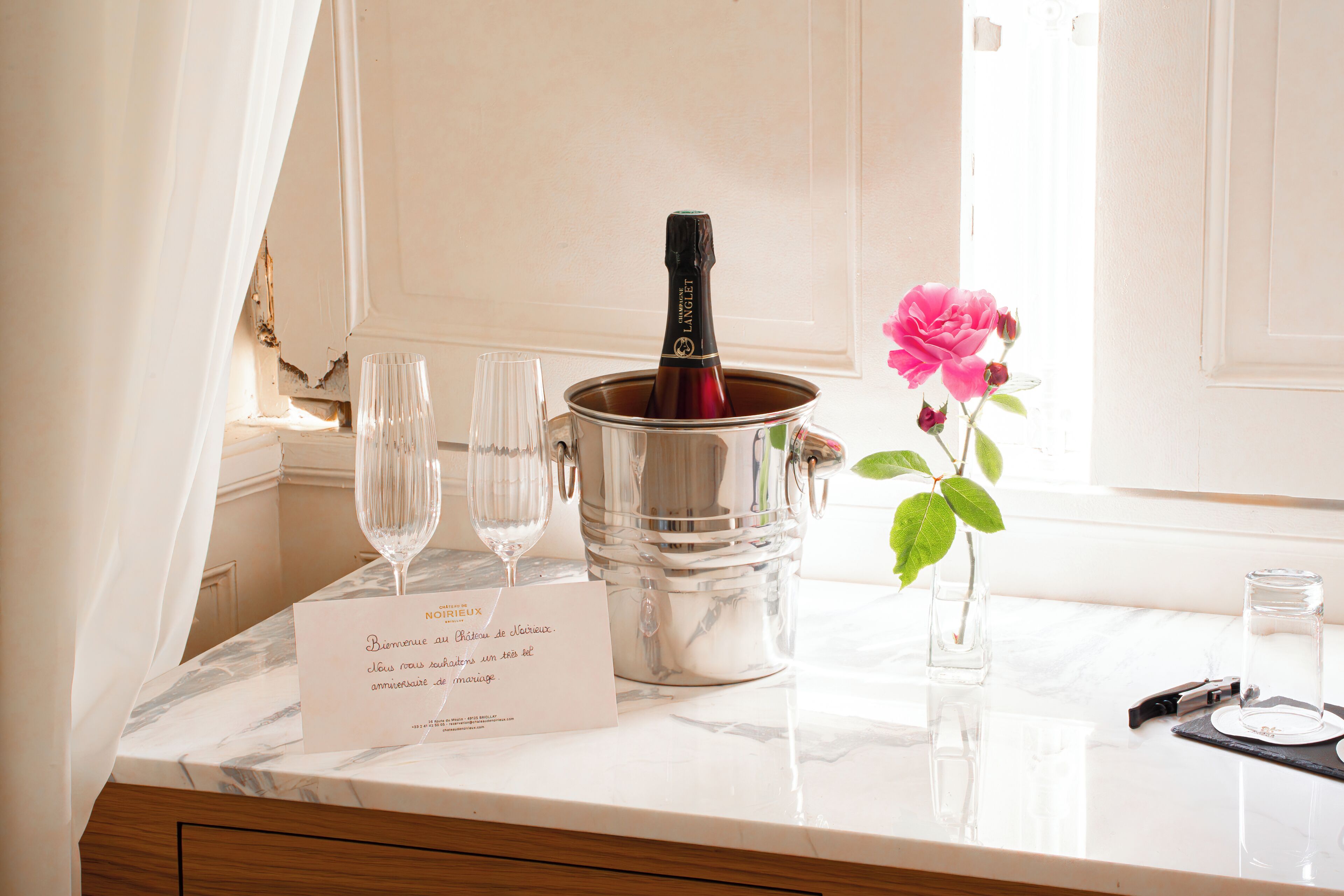 A marble countertop with a champagne bottle, two glasses, a flower vase, and a menu.