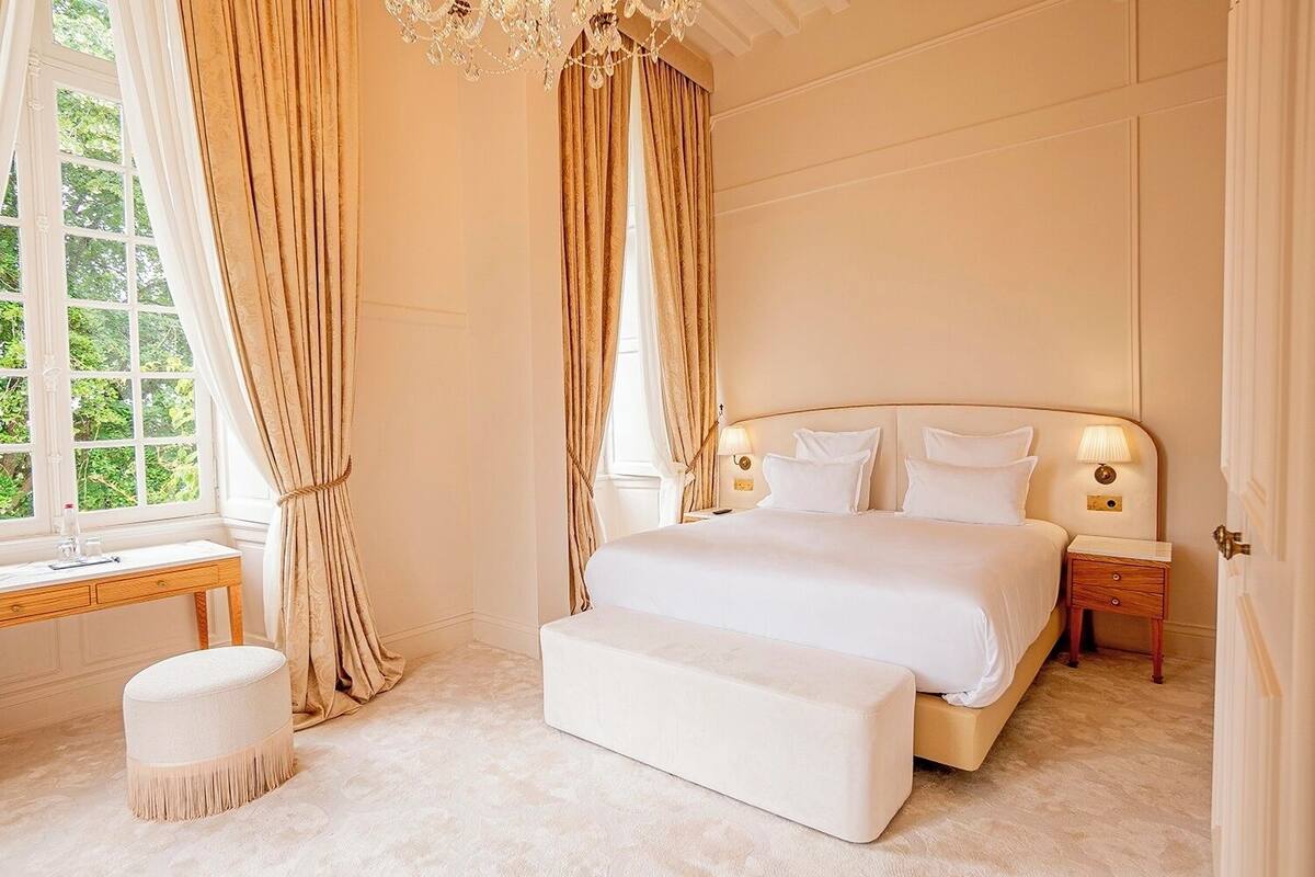 Ein geräumiges Schlafzimmer mit einem großen Bett, einem Nachttisch, Vorhängen und einem Fenster.