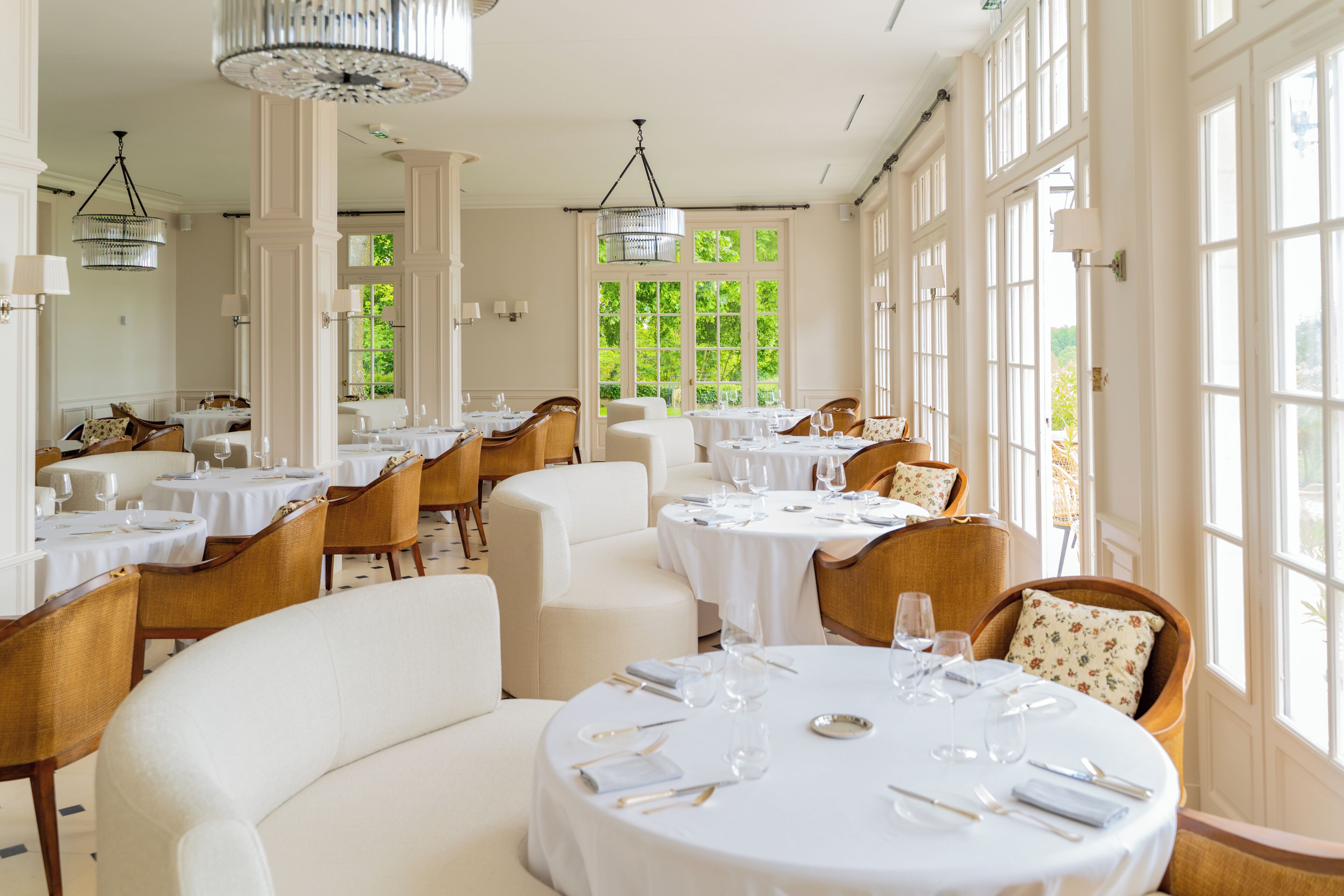 A dining area with round tables, white tablecloths, and wooden chairs.