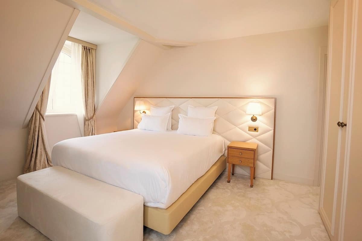 Ein Schlafzimmer mit einem großen Bett, einem Nachttisch, einer Bank und einem Fenster mit Vorhängen.