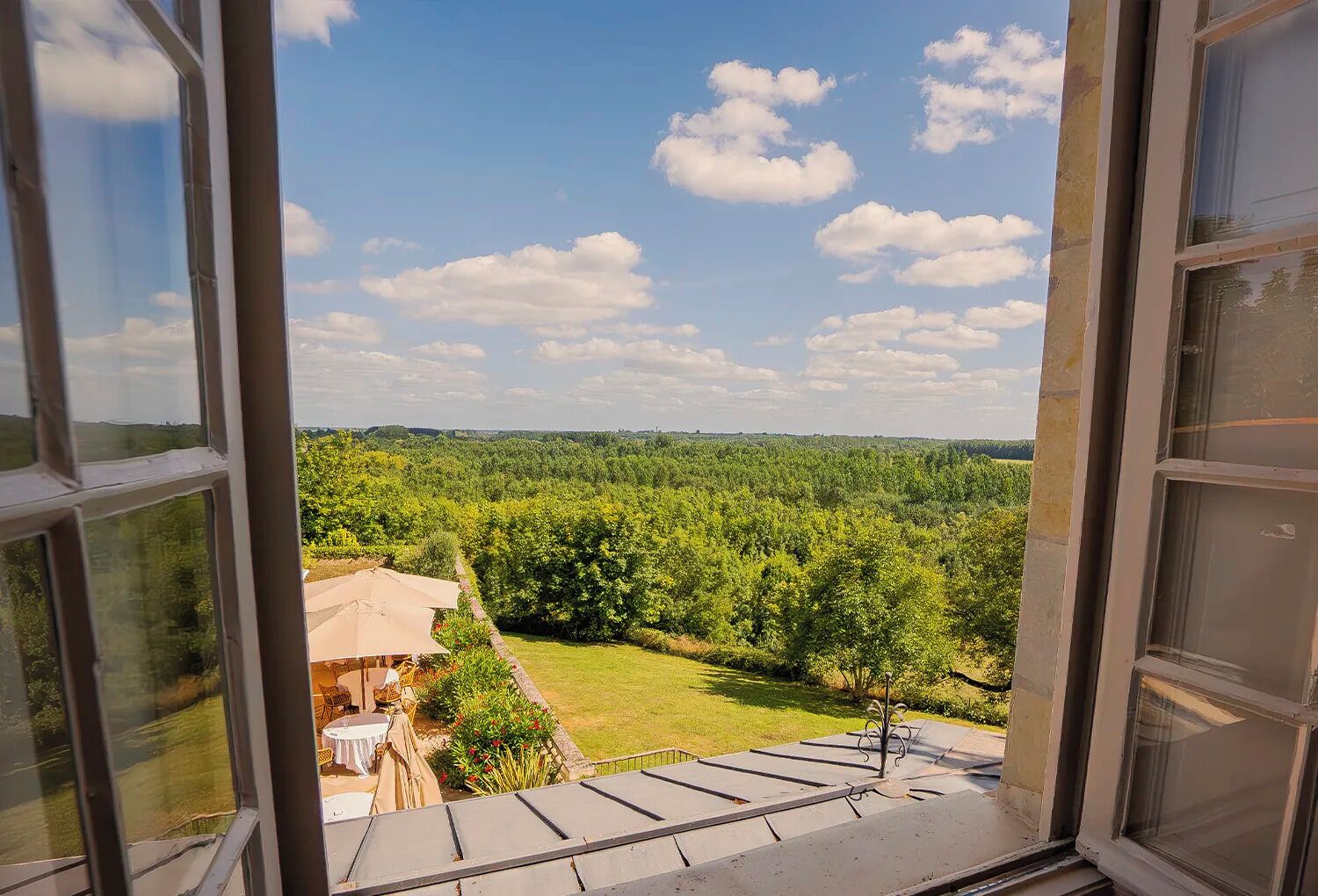 Blick aus einem Fenster auf eine üppige grüne Landschaft unter blauem Himmel.