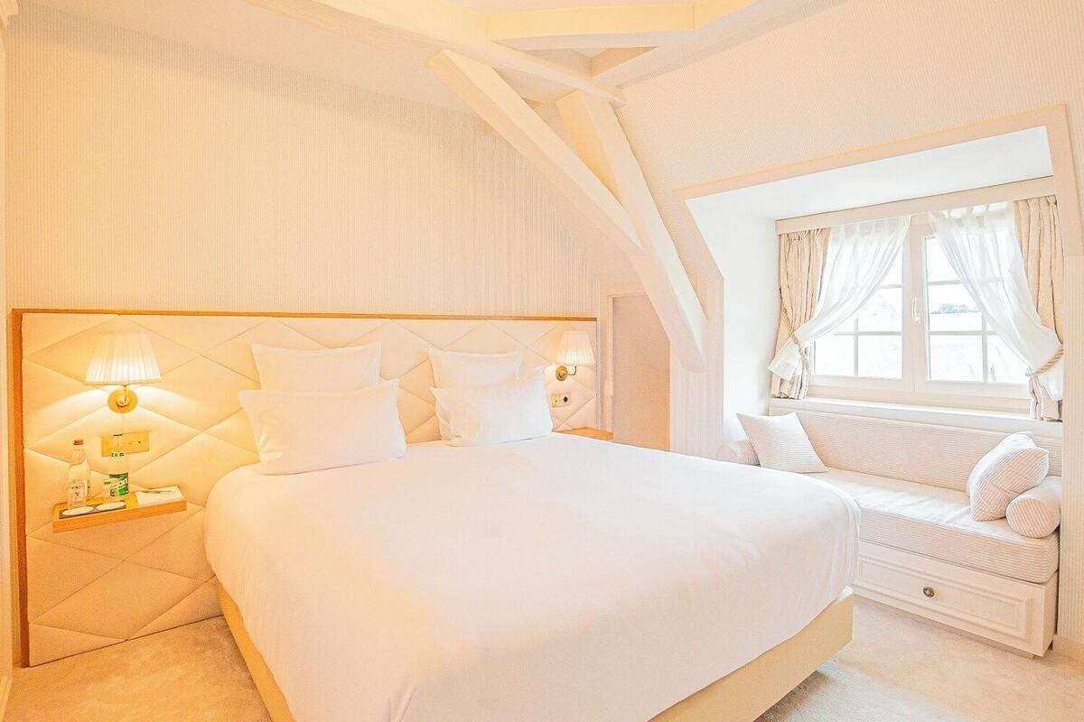 Ein geräumiges Schlafzimmer mit einem großen Bett, einem Nachttisch mit Lampe und einem Fenster mit Vorhängen.
