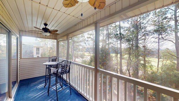 A covered porch with a table and chairs, large windows, and a ceiling fan. - Secluded Paradise Serene 2BR Golf Course Views (Pawleys Island)