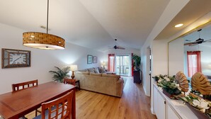 A spacious living area with a wooden dining table, a sofa, and a ceiling fan. - Secluded Paradise Serene 2BR Golf Course Views (Pawleys Island)