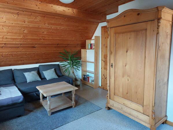 Ein gemütliches Wohnzimmer mit Holzboden, einer Couch mit Kissen, einem Couchtisch, einem großen Holzschrank und einem Bücherregal mit Büchern.