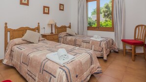 Ein Hotelzimmer mit zwei Betten, einem Holzstuhl, einem Fenster mit Vorhängen und einem kleinen Tisch mit Lampe.