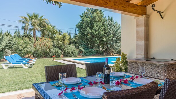 Ein Essbereich im Freien mit Blick auf einen Pool, Korbmöbeln und einem Grill.