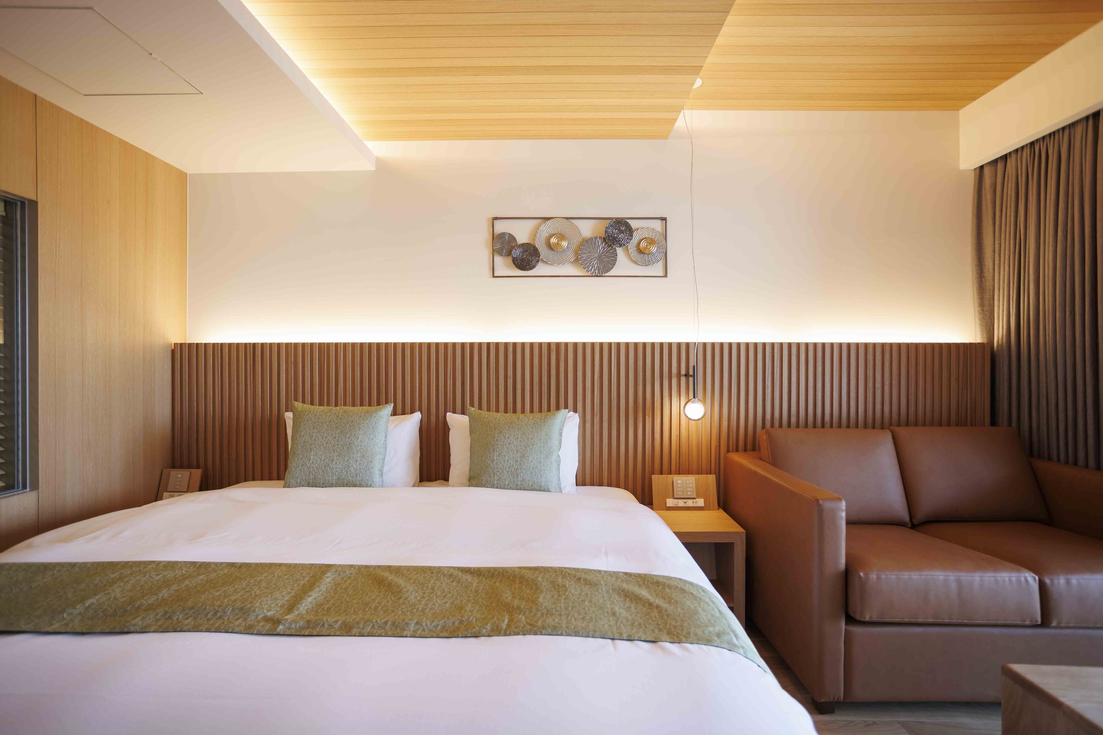 Una habitación de hotel con una cama grande, un sofá, una mesita de noche con lámpara y un adorno en la pared.
