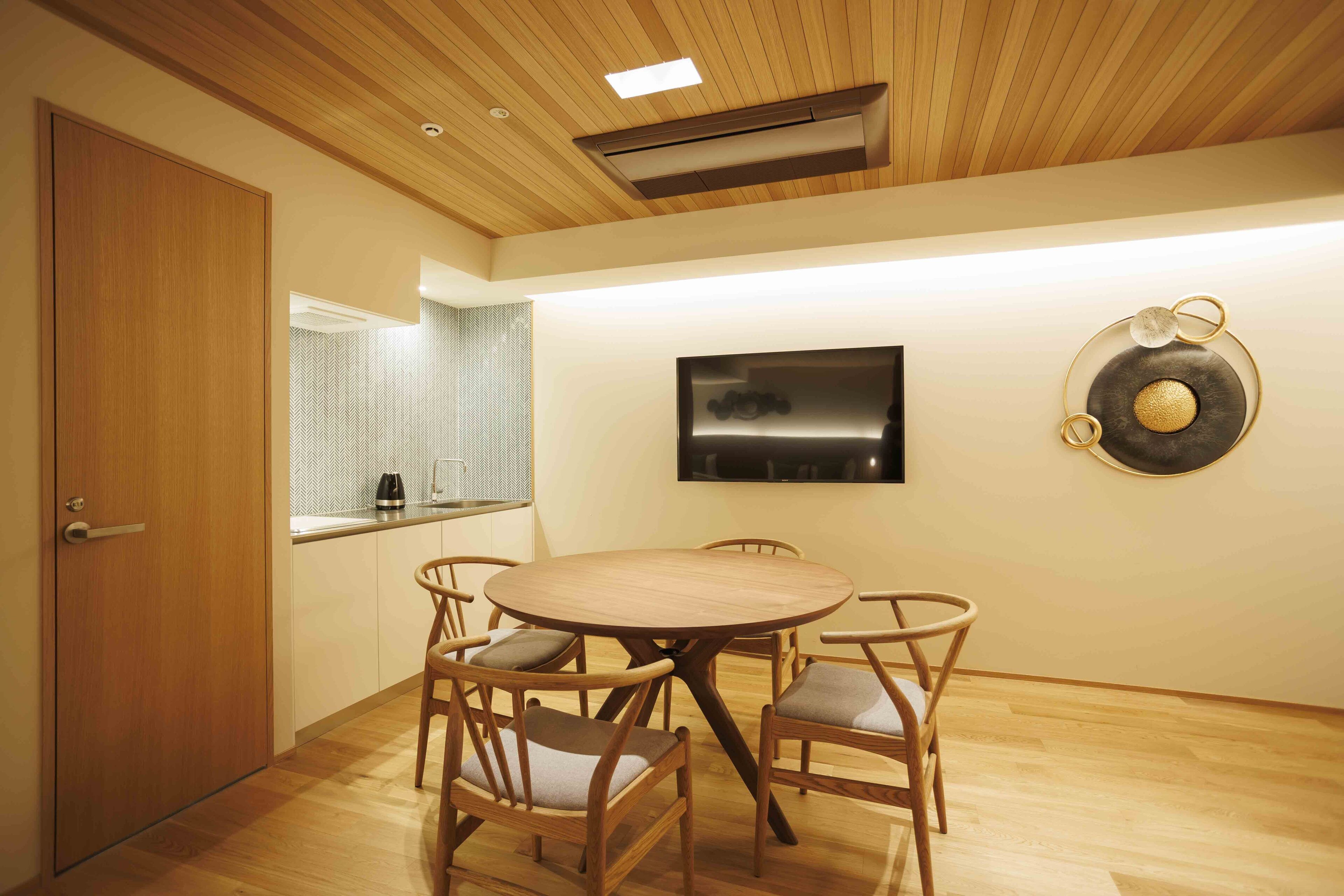 A dining area with a round wooden table and six chairs, a TV mounted on the wall, and a decorative wall piece.