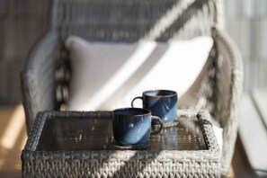 Una silla de mimbre con una bandeja que sostiene dos tazas de cerámica.