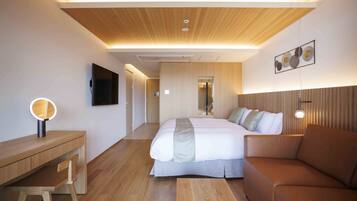 A modern hotel room with a wooden ceiling, a bed with a grey bedspread, a brown leather sofa, a wooden desk with a chair, and a wall-mounted TV.