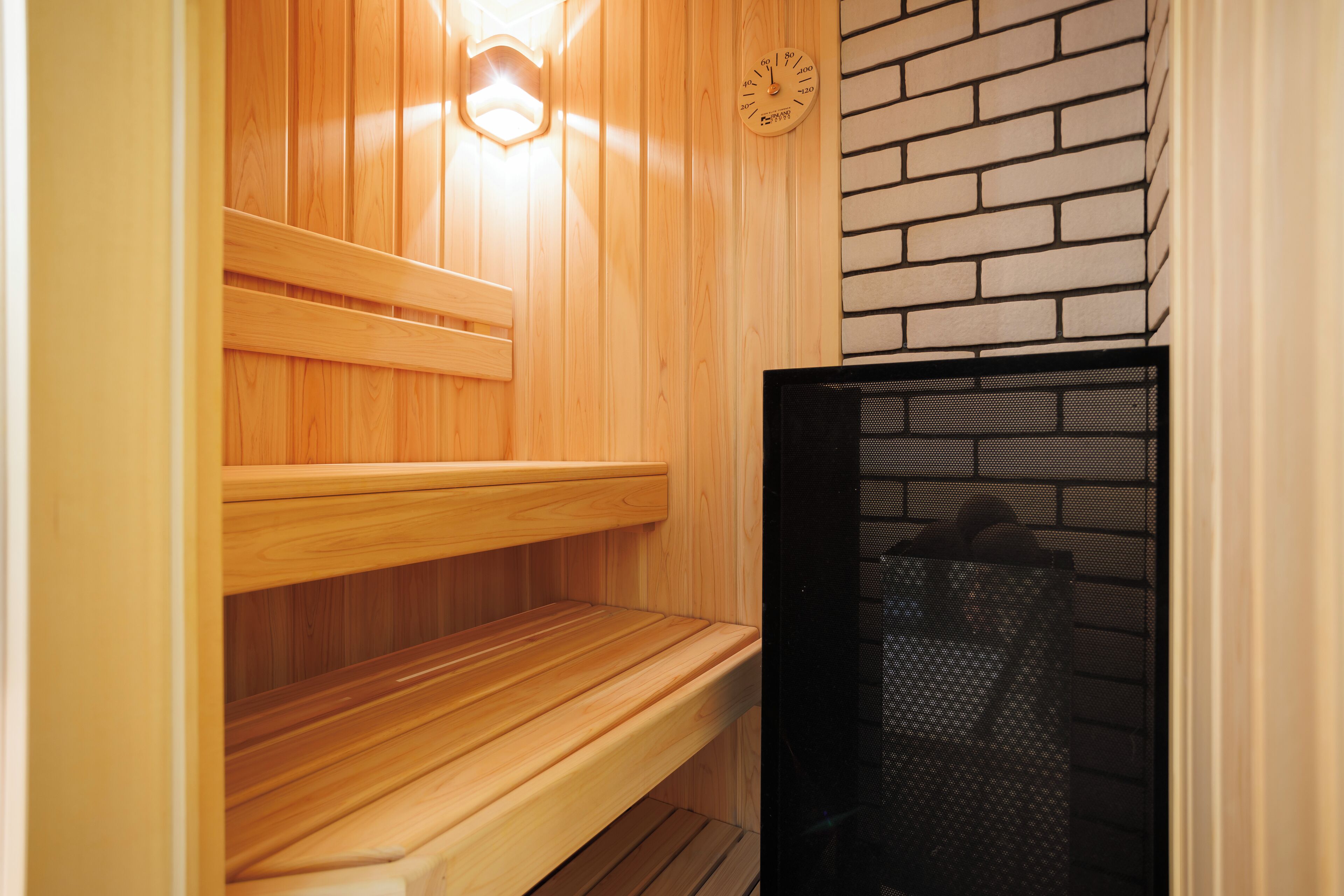 A wooden sauna with benches and a black mesh door.