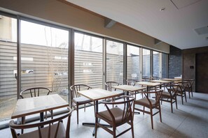 Un comedor con varias mesas y sillas, ventanas amplias y vistas al exterior.