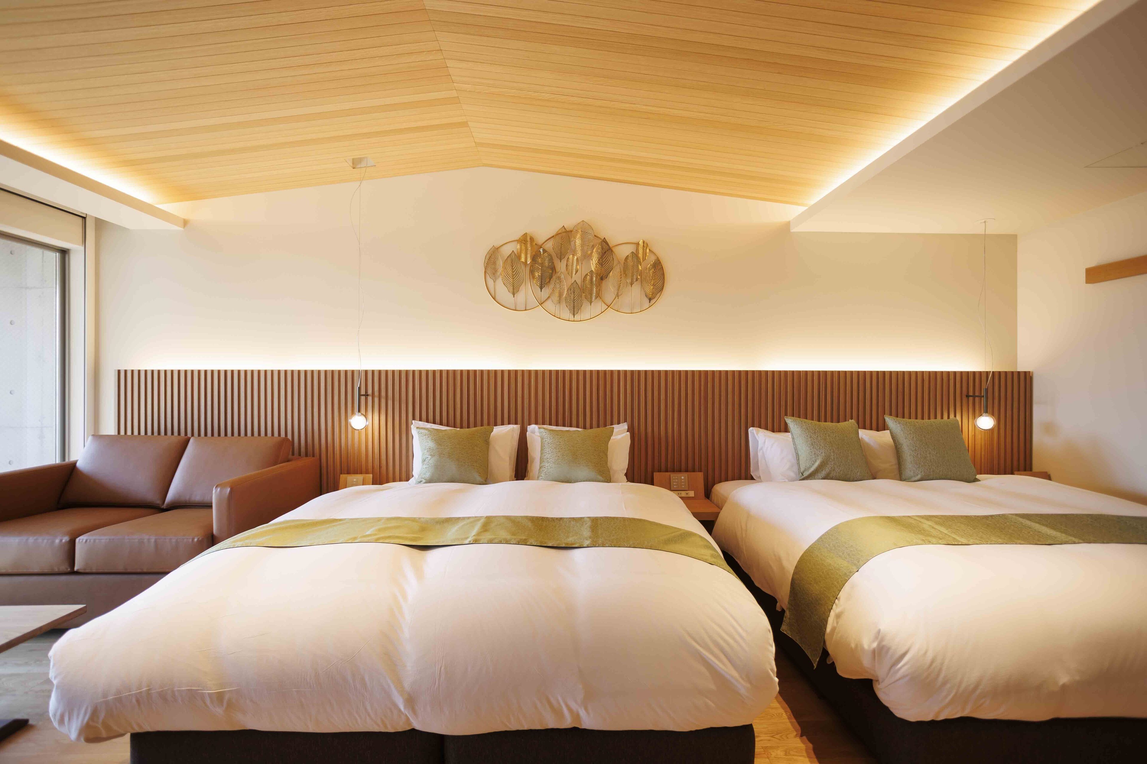 A modern hotel room with two beds, a wooden ceiling, and a wall-mounted light fixture.