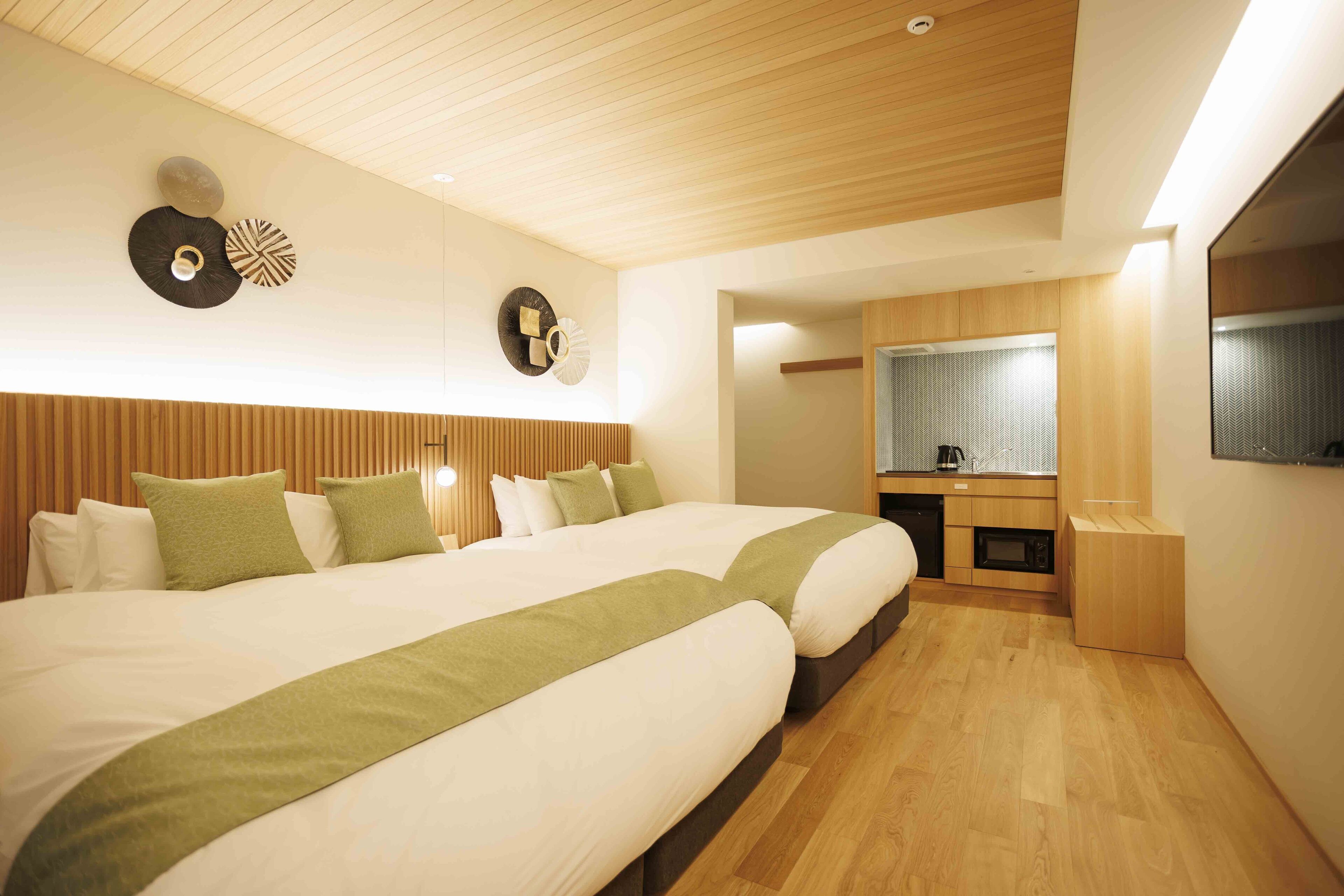 Habitación de hotel con dos camas, techo de madera, kitchenette y un espejo grande.