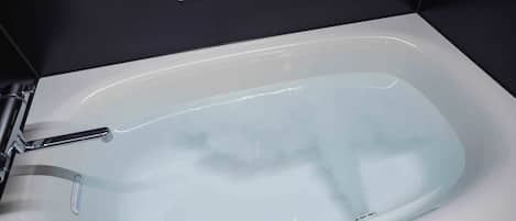 Un baño moderno con una bañera blanca, un grifo cromado y un panel de control por encima de la bañera.