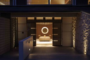 Vestíbulo moderno de hotel con diseño minimalista, que presenta una zona de camas central con una lámpara circular suspendida sobre ella.
