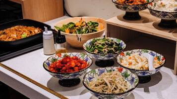 Une table de buffet proposant divers plats présentés dans des bols, notamment des salades, des nouilles et des légumes sautés.