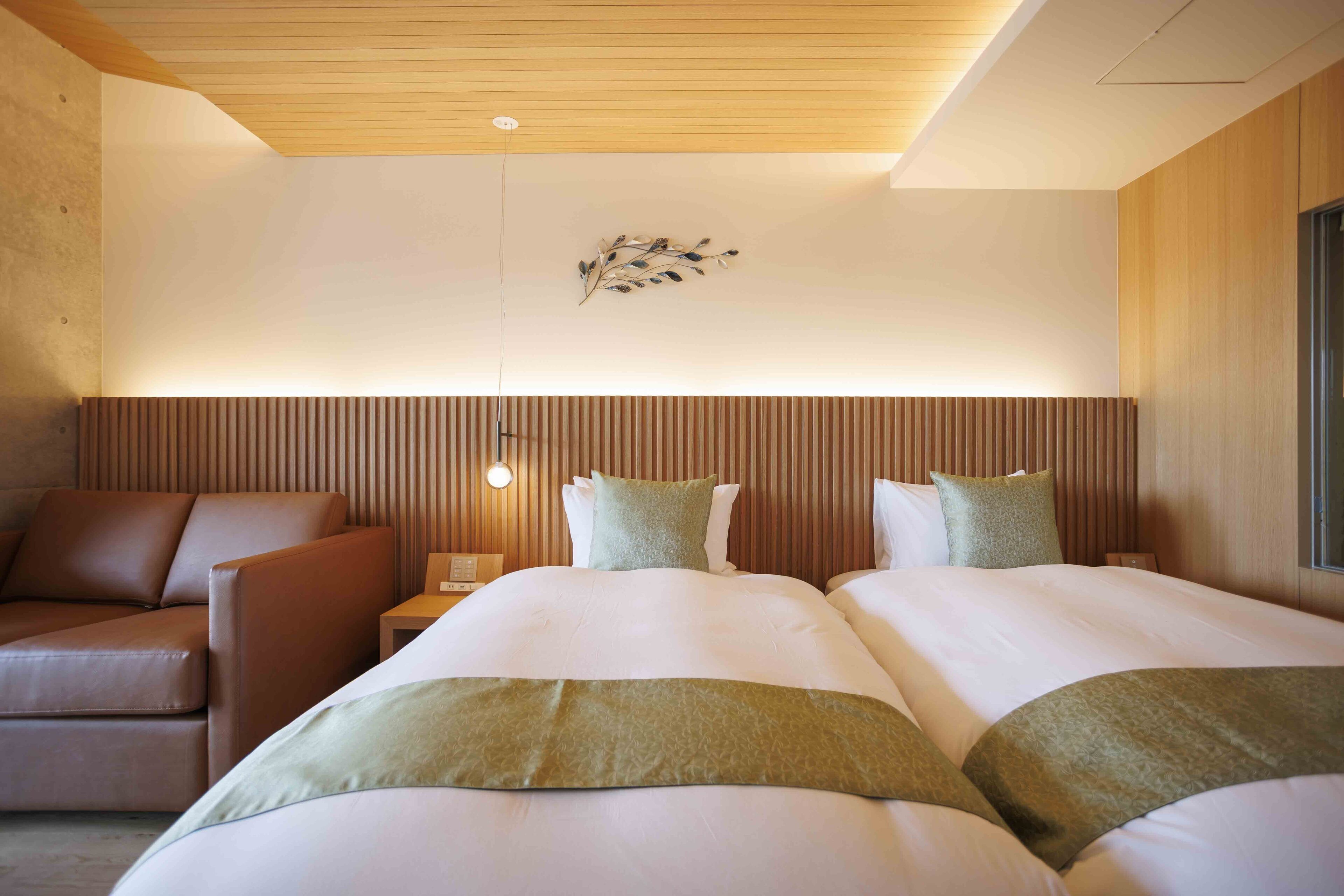 Een hotelkamer met twee bedden, een bank, een houten plafond en een wandlamp.