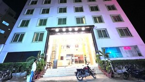 A multi-story hotel with a brightly lit entrance, a staircase leading to the lobby, and several motorcycles parked outside. - HOTEL SM RAINBOW INTERNATIONAL (Hyderabad)