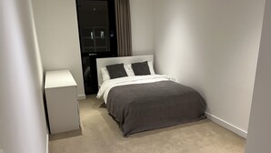 Une chambre à coucher comprenant un lit, une table de chevet et une porte donnant sur un couloir.