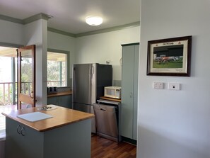 A compact kitchen with a refrigerator, microwave, and dishwasher. There is a framed picture on the wall and a window with a view of greenery.