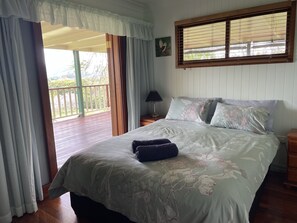 A bedroom with a bed, a nightstand, a window with blinds, and a balcony view.
