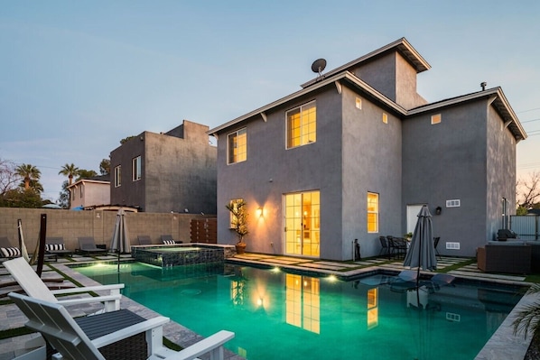 Una casa moderna con piscina, sillas de descanso y un patio.