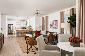 A modern living room with a dining area, kitchen, and a ceiling fan.