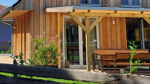 A two-story wooden house with a balcony, large windows, and a covered patio area. - Dogs and children welcome, 150m to the beach, fenced property,  (Rheinsberg OT Flecken Zechlin)