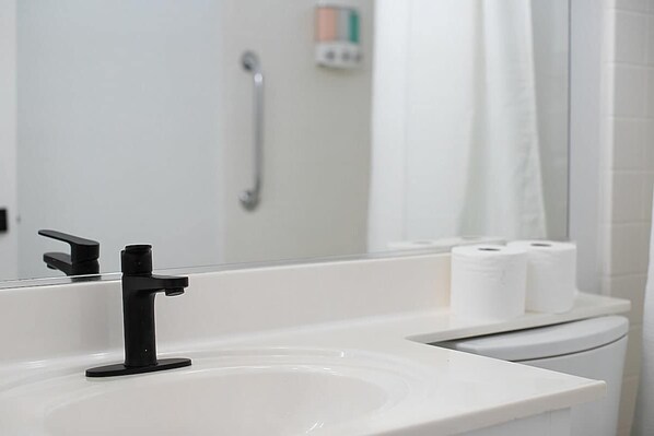 A bathroom with a white sink, black faucet, and a mirror reflecting a shower area.