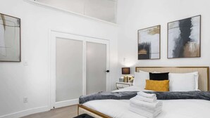A modern bedroom with a large bed, a black ottoman, and artwork on the walls. - 4BR Pool, Spa & Retro Arcade Polished Vegas Stay (North Las Vegas)