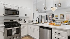 A modern kitchen with white cabinetry, stainless steel appliances, and a central island with a sink and countertop. - 4BR Pool, Spa & Retro Arcade Polished Vegas Stay (North Las Vegas)