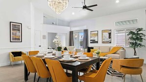 A modern dining area with a central table set for six, surrounded by yellow chairs. There is a ceiling fan above, and the room has a clean, minimalist design with white walls and a large window. - 4BR Pool, Spa & Retro Arcade Polished Vegas Stay (North Las Vegas)