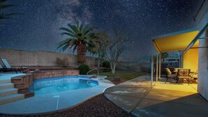 A swimming pool with a stone edge, a palm tree, and a covered patio area with outdoor furniture. - 4BR Pool, Spa & Retro Arcade Polished Vegas Stay (North Las Vegas)