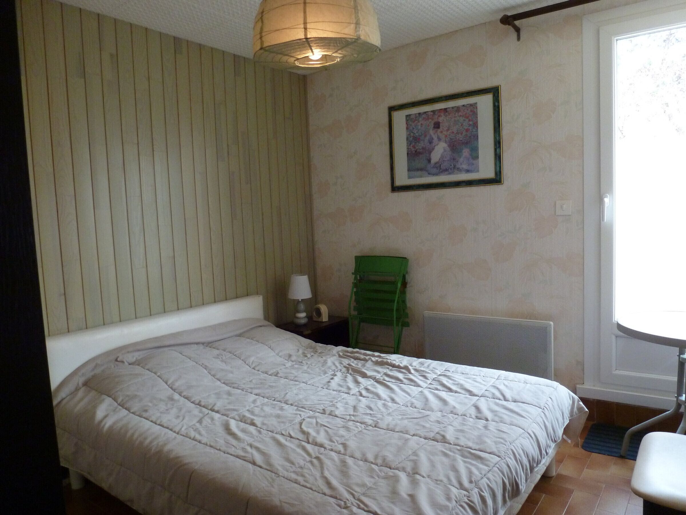 Een slaapkamer met een bed, een groene stoel, een lamp en een schilderij aan de muur.