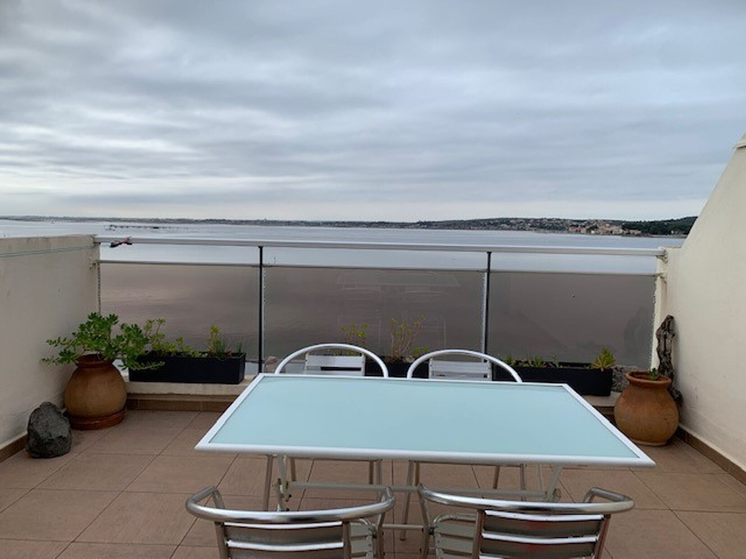 A rooftop terrace with a table and chairs, potted plants, and a view of the sea.