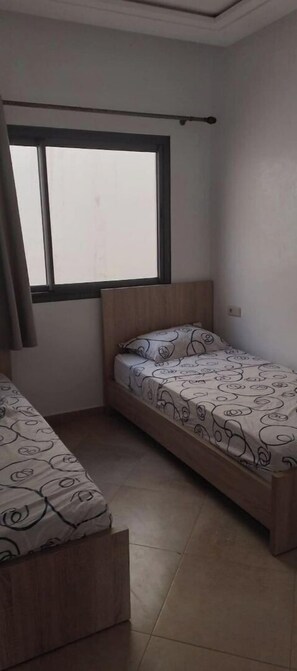 A small, clean room with two single beds, a window, and a curtain. - Beach and surf lovers (Aourir)