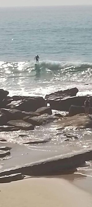 A rocky beach with waves and a person surfing. - Beach and surf lovers (Aourir)